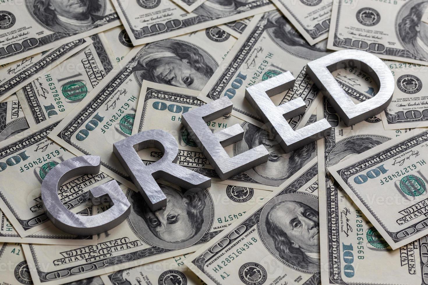 The word GREED laid with aluminium letters on the US dollar banknotes background - with selective focus photo
