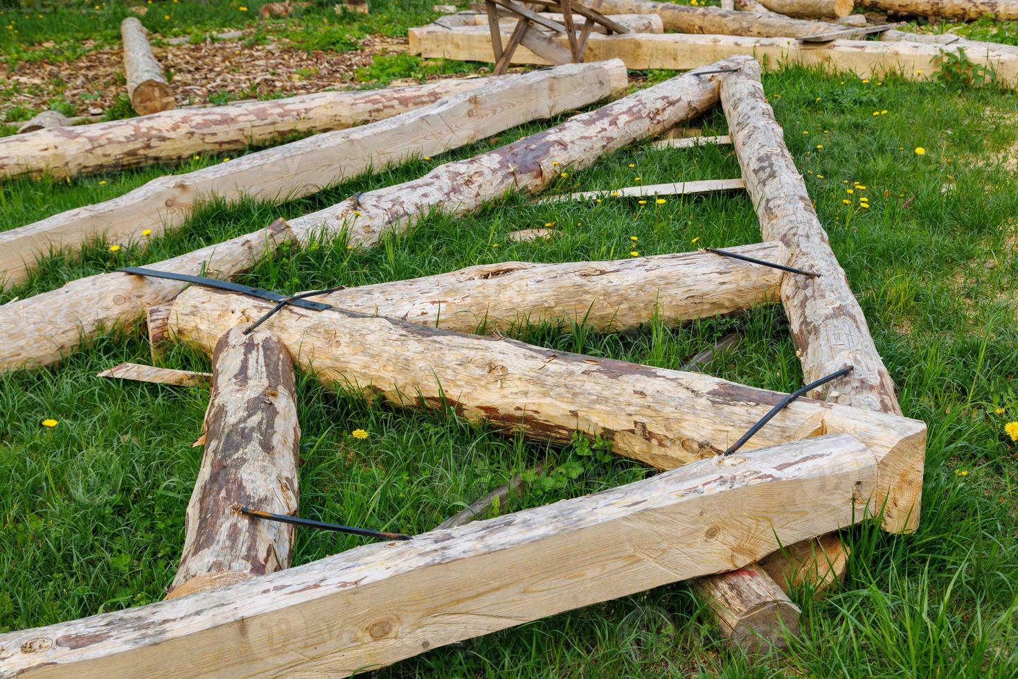 forged steel stripe connection of wooden log beams for roof support girder framework laid on green grass at summer day photo