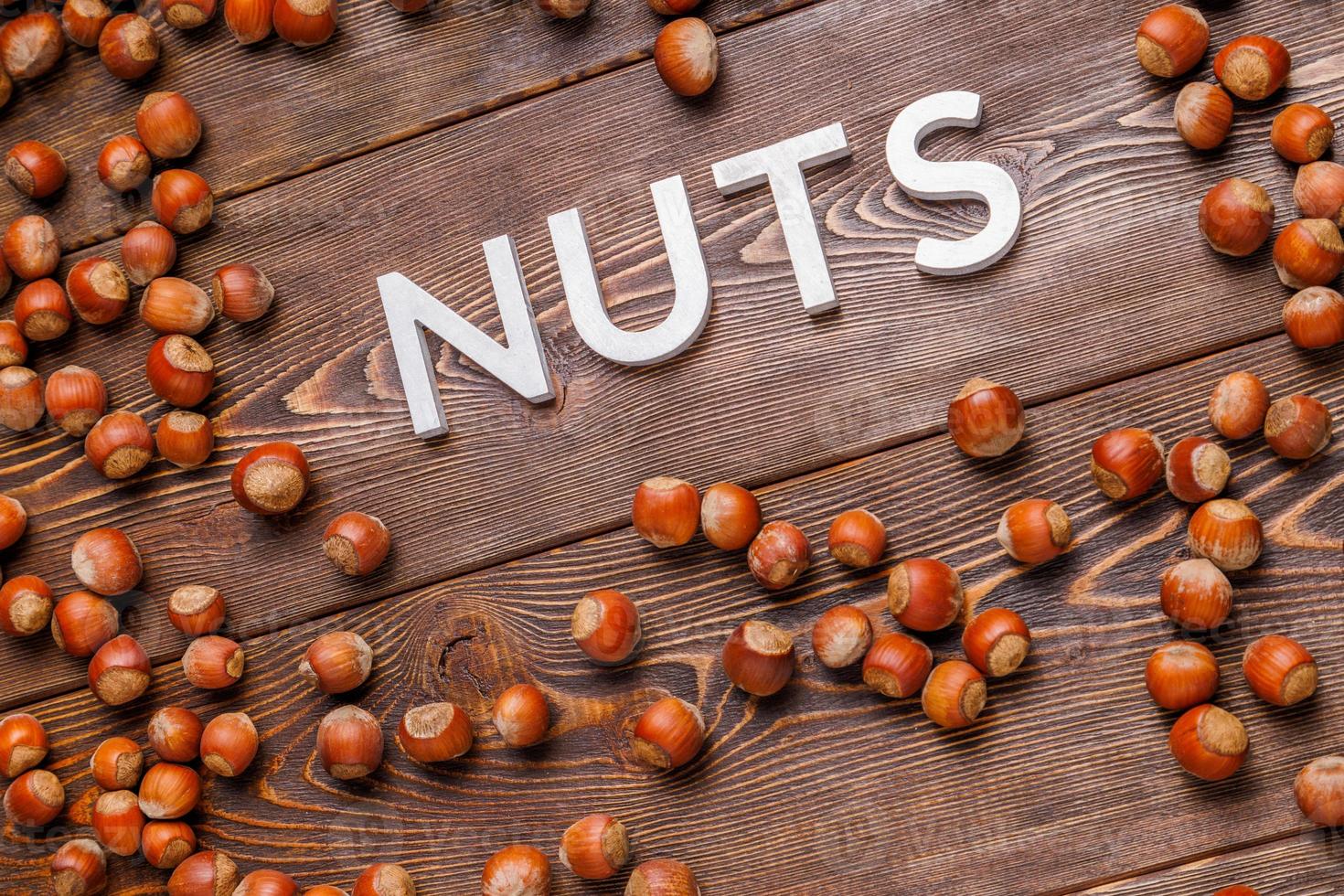 the word nuts laid with silver letters on wooden board background surrounded with scattered hazelnuts photo