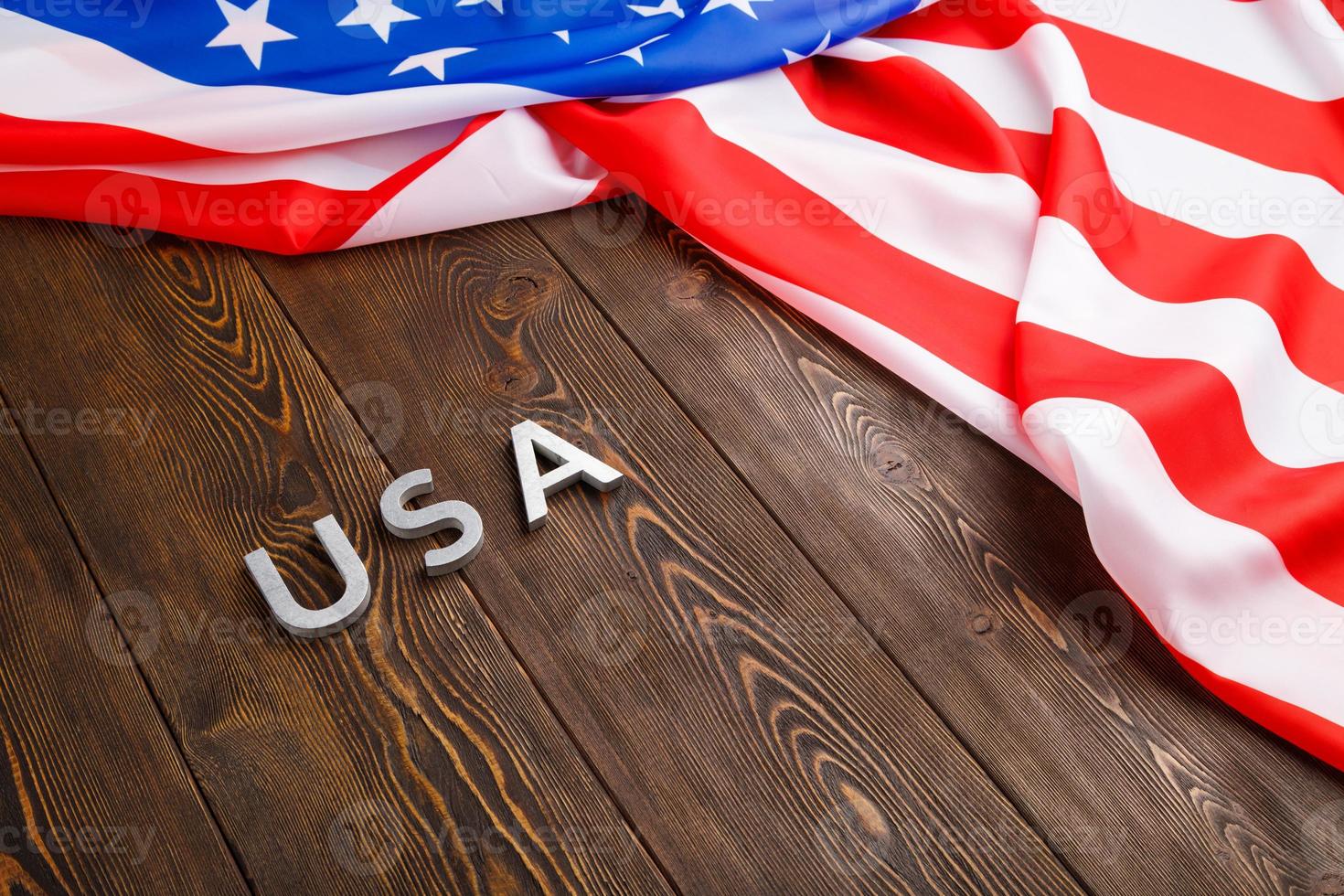 the word USA laid with silver metal letters on wooden board surface under crumpled flag of United States of America photo