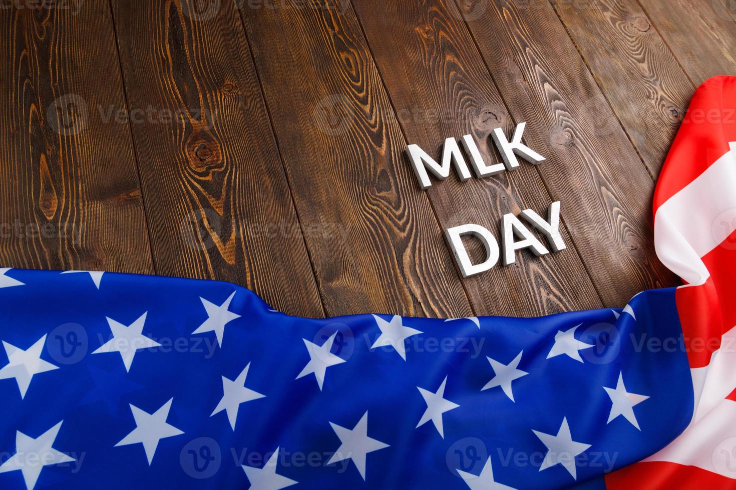 the word MLK day laid with silver metal letters on wooden surface with crumpled USA flag underneath photo