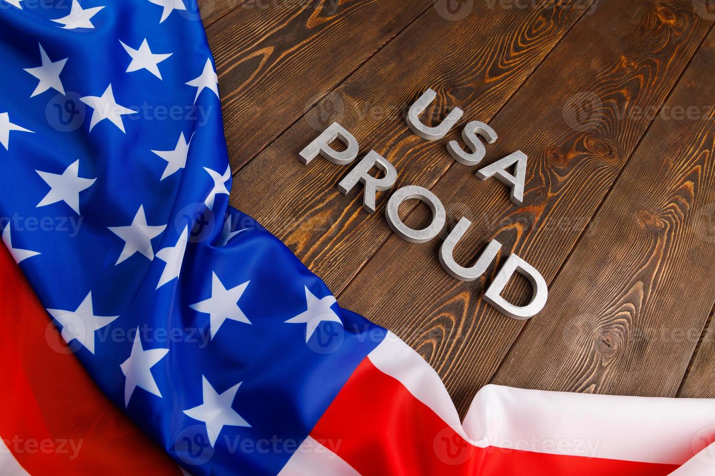 words USA proud laid with silver metal letters on brown wooden surface with flag of United States of America photo