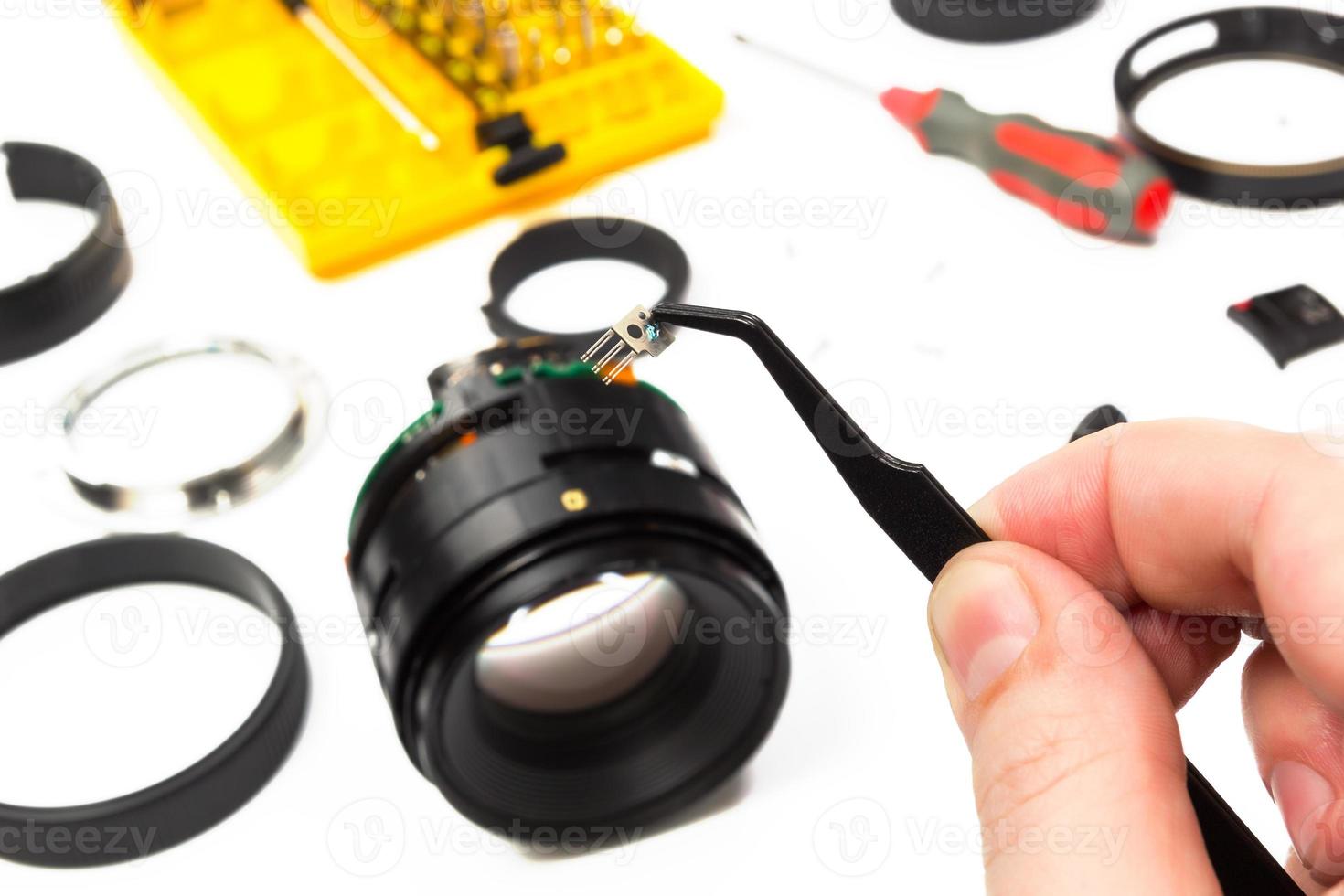 Hand with tweezers holding part of camera lens photo