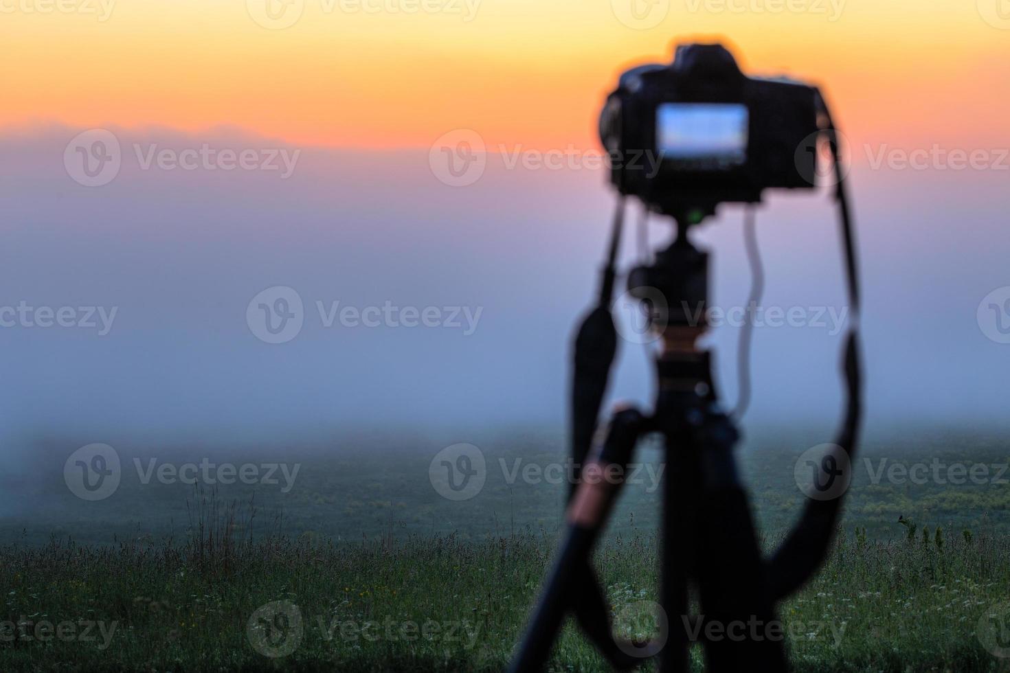 black digital camera on tripod shooting foggy morning landscape at summer with selective focus photo