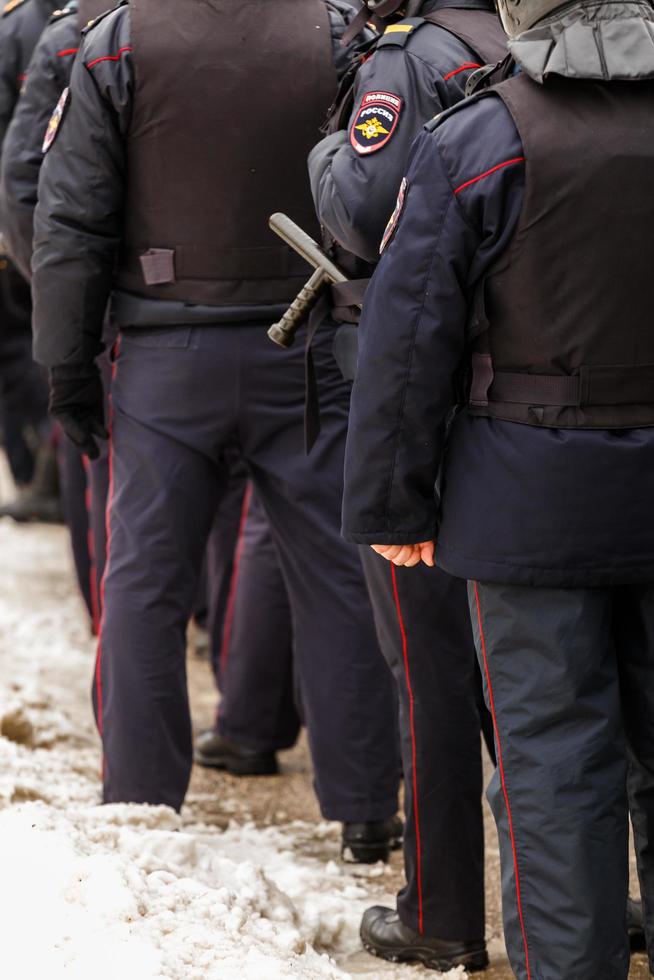 Tula, Russia  January 23, 2021 Crowd of police officers in black uniform with bulletproof vests and pistols - view from back. photo