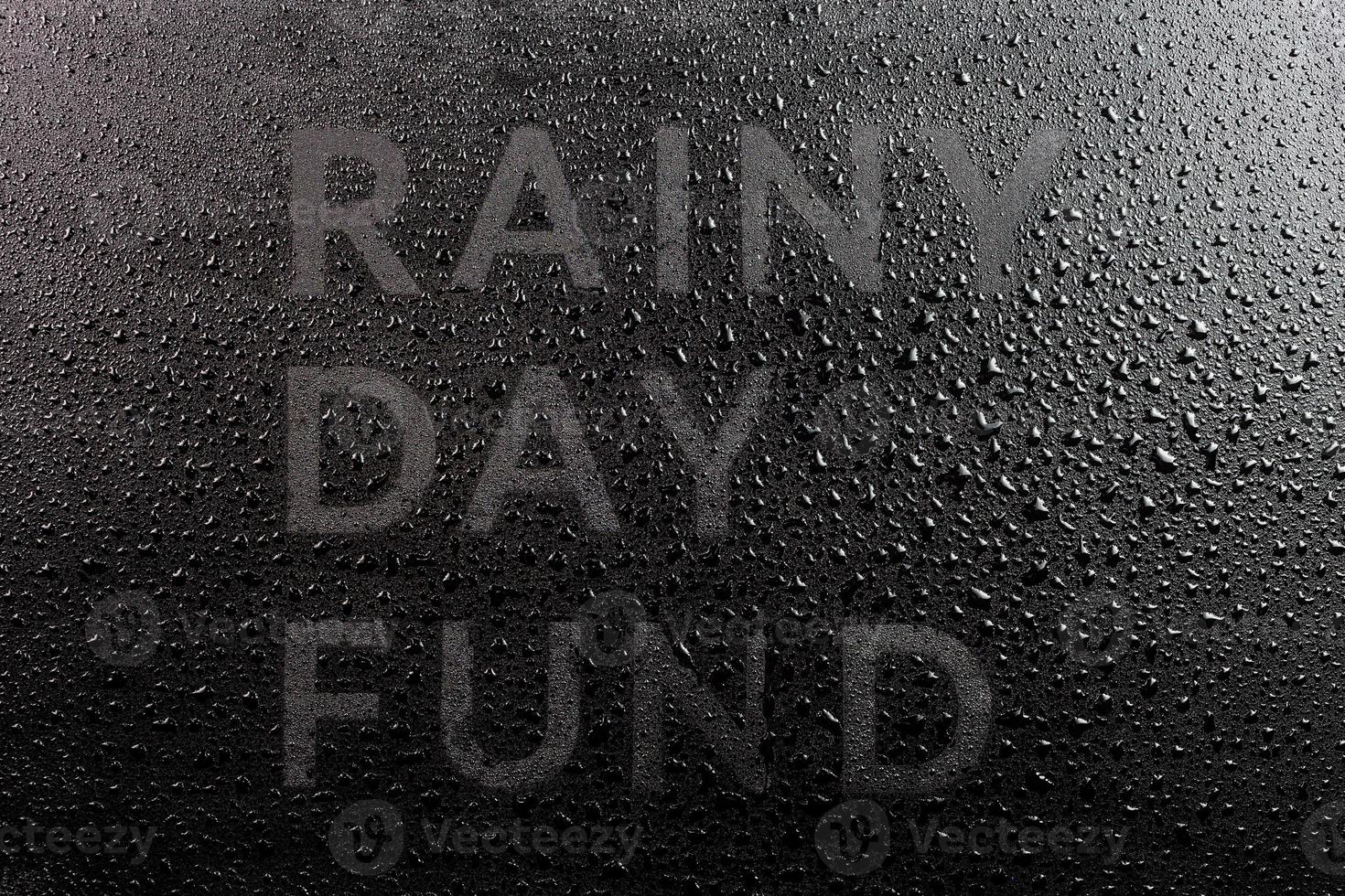 the dry words rainy day fund covered from water drops on black surface, unusual implementation concept in flat lay perspective photo