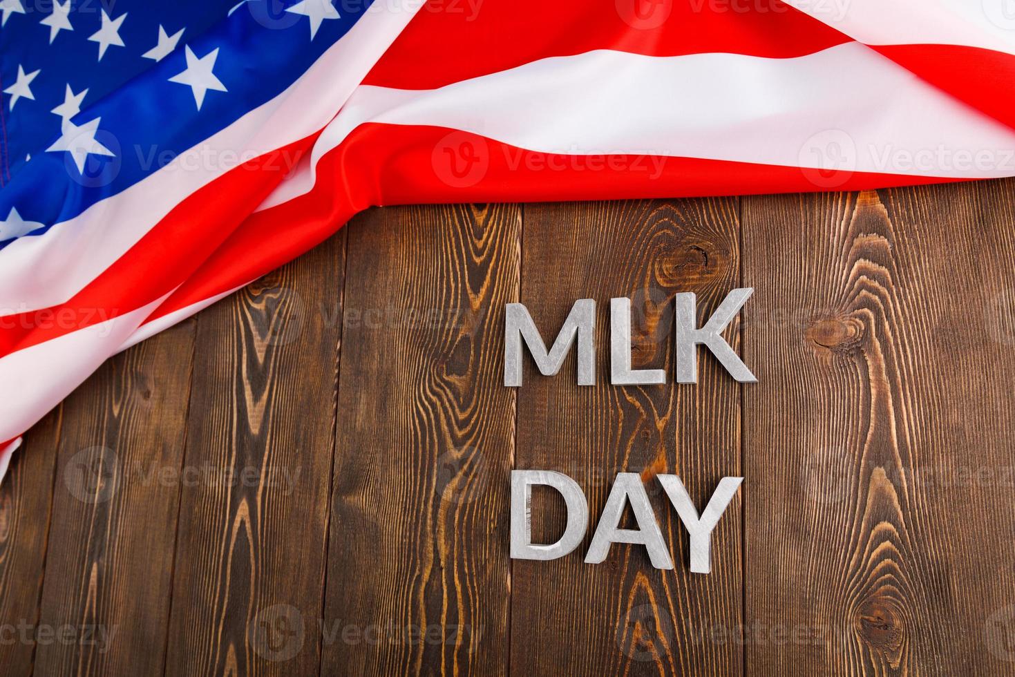 la palabra mlk day colocada con letras de metal plateado sobre una superficie de madera con una bandera de estados unidos arrugada en la parte superior foto