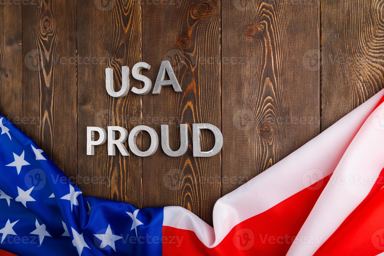 words USA proud laid with silver metal letters on brown wooden surface with flag of United States of America photo