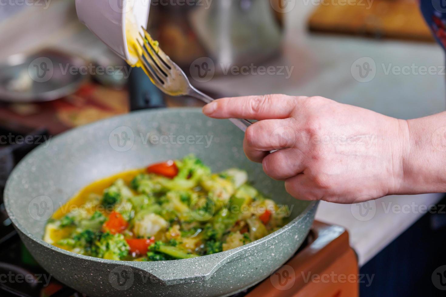 female hands adds a scrambled egg yolks to frying vegetables while cooking omelette photo