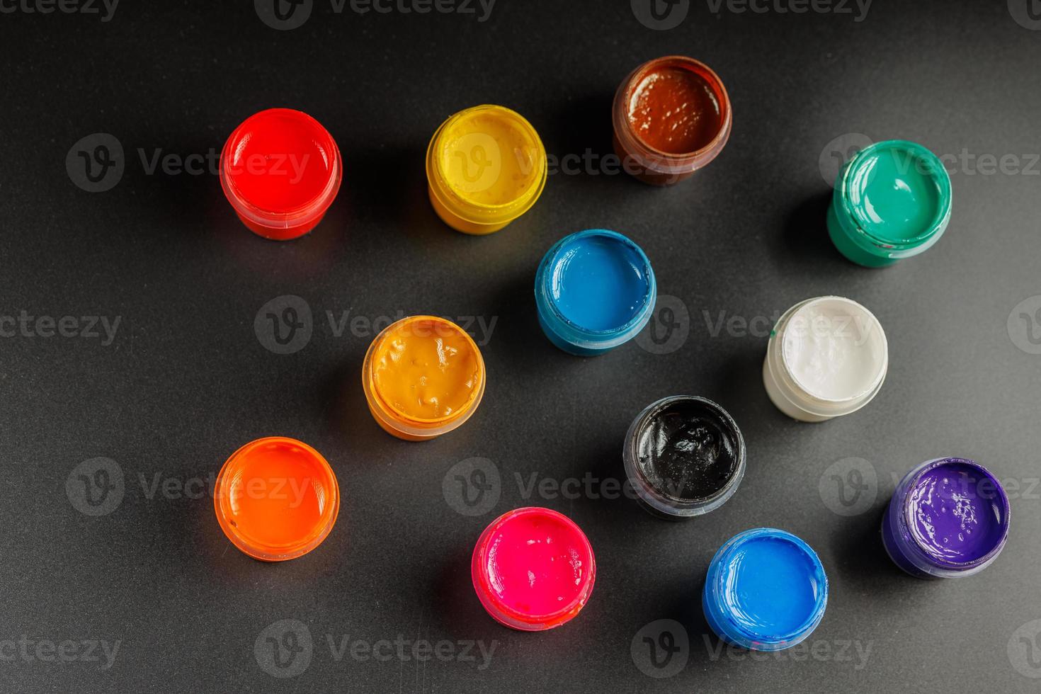 close-up background of opened small gouache paint jars on black surface photo