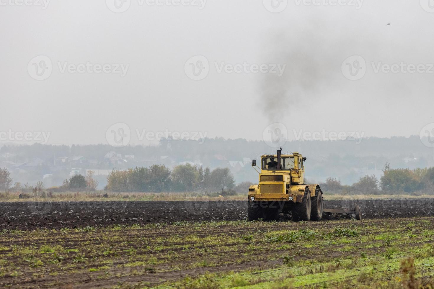 el tractor amarillo sombrío ara el campo después de la cosecha antes del invierno en la mañana nublada y nublada del otoño foto