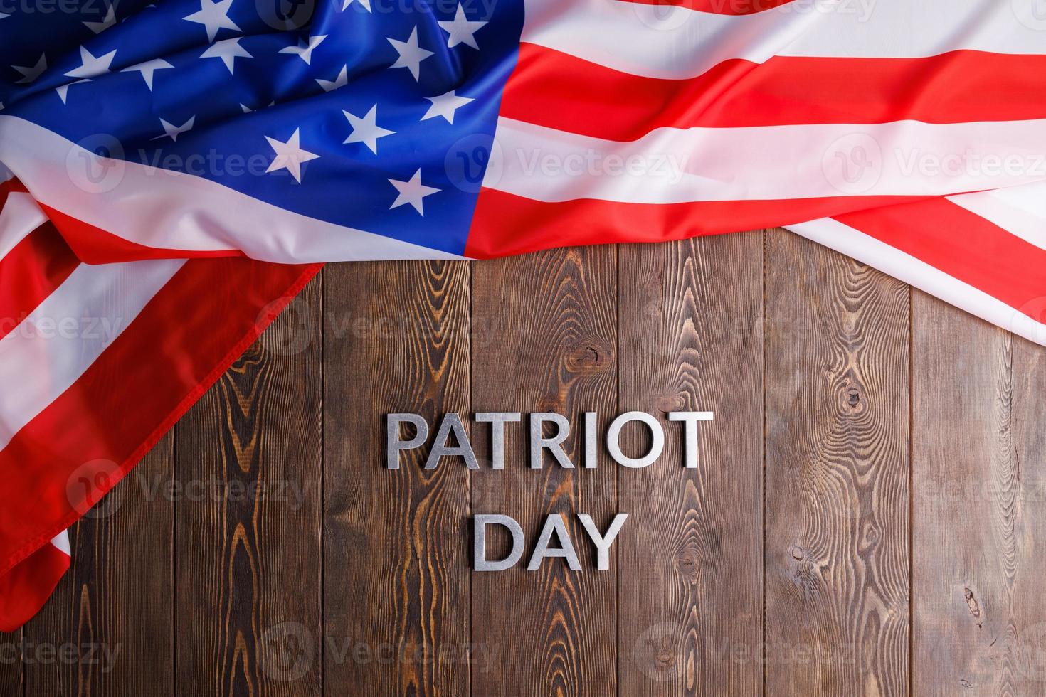 the words patriot day laid with silver metal letters on wooden board surface with crumpled usa flag photo