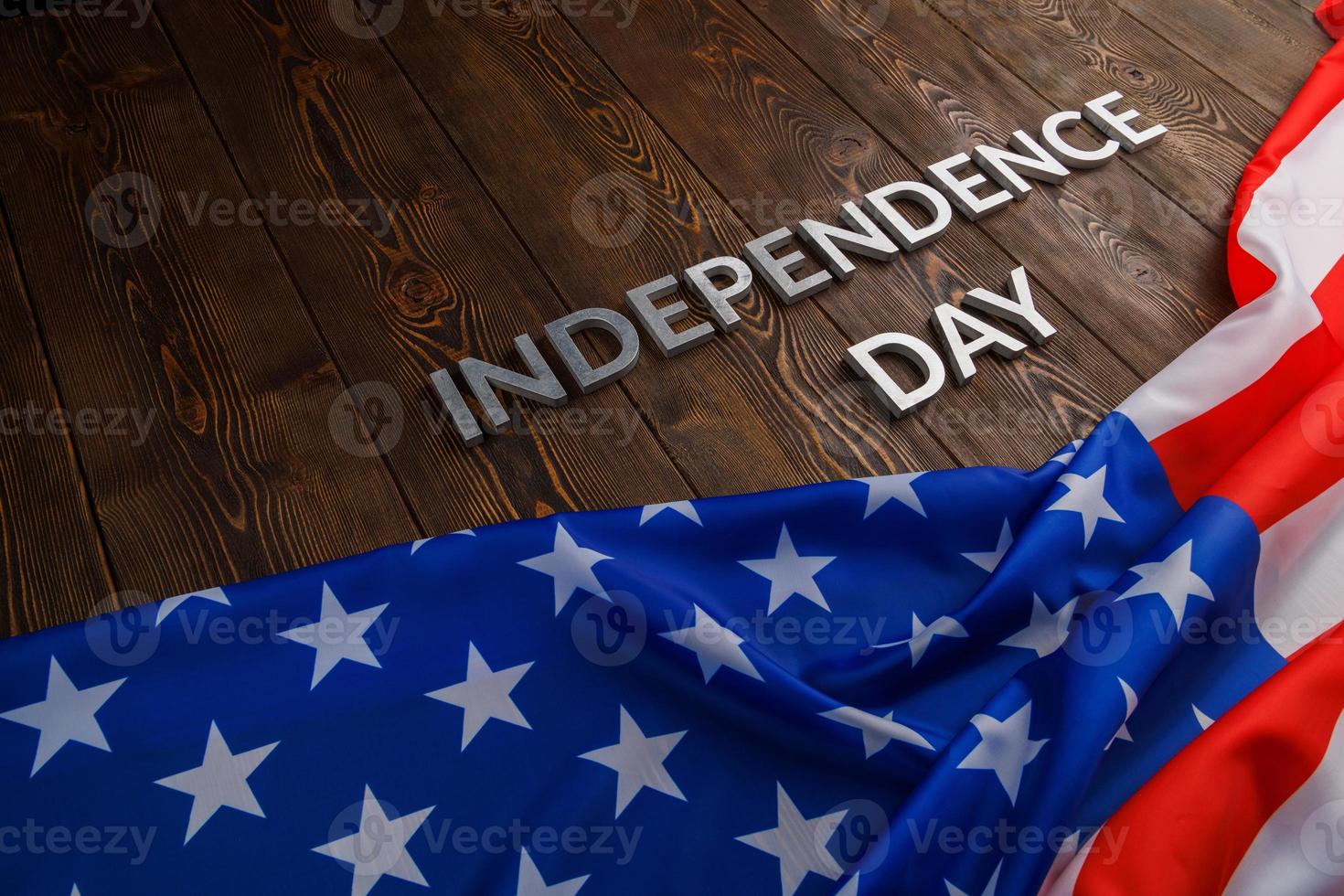 las palabras día de la independencia colocadas en la superficie de tablones de madera marrón con la bandera de los estados unidos de américa arrugada foto