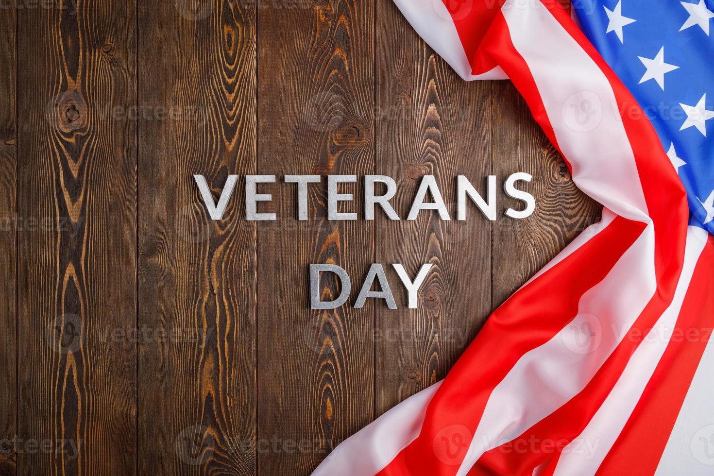 the words veterans day laid with silver metal letters on wooden board surface with crumpled usa flag photo