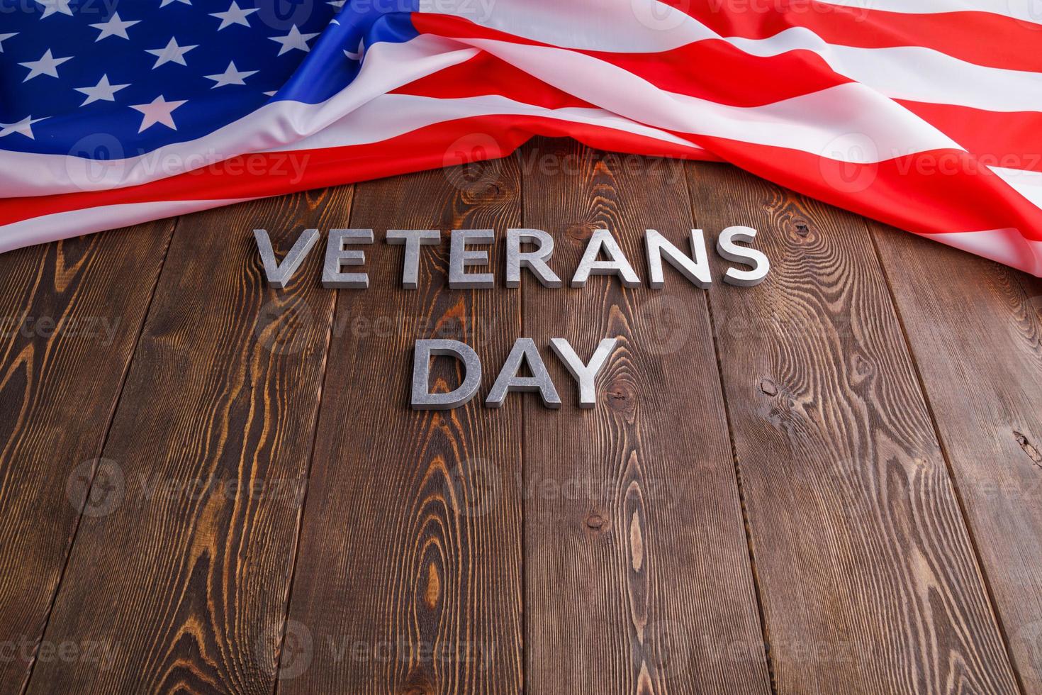 the words veterans day laid with silver metal letters on wooden board surface with crumpled usa flag photo
