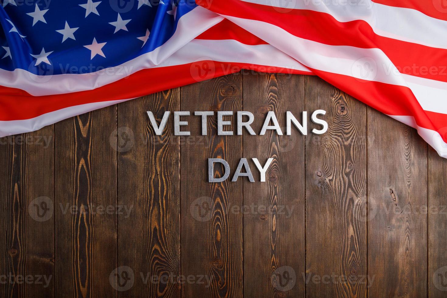 the words veterans day laid with silver metal letters on wooden board surface with crumpled usa flag photo