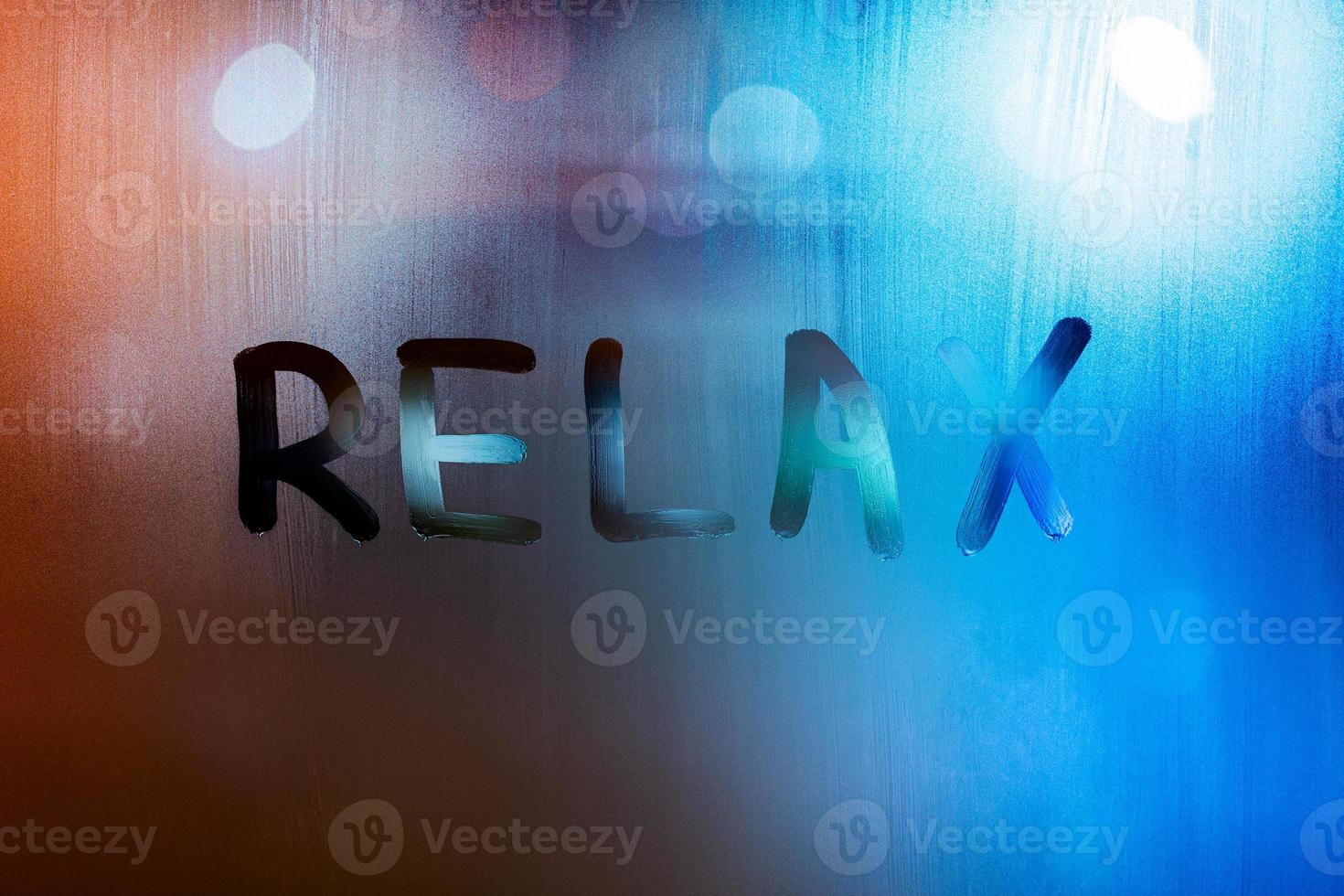 the word relax written by finger on wet glass with blurred lights in background photo