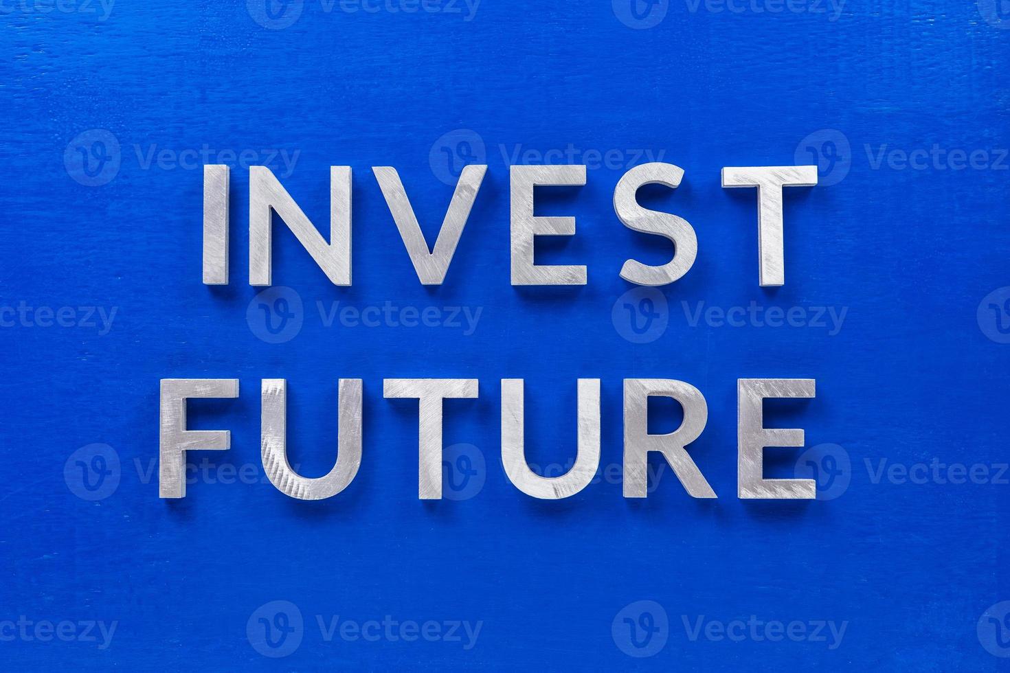 the words invest future laid with silver metal characters on blue painted wooden board in central flat lay composition photo