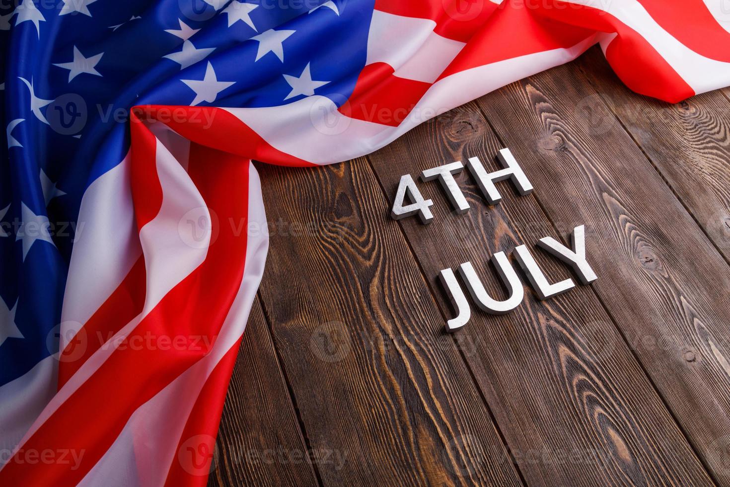 the words 4th july and crumpled usa flag on flat textured wooden surface background photo