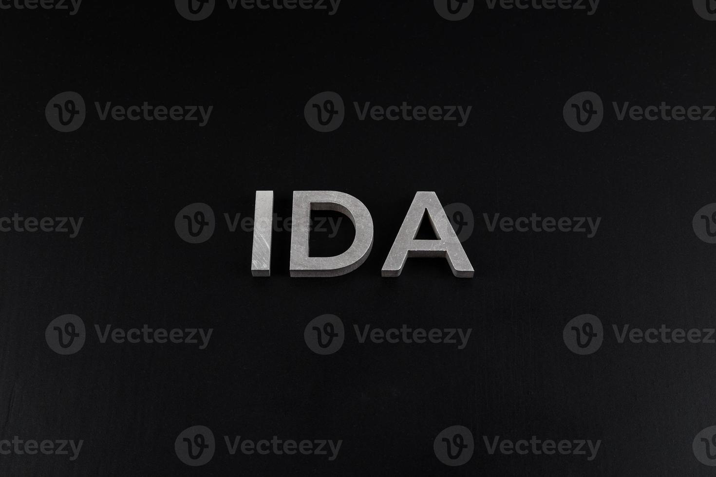 the word ida laid with silver metal letters over dry black matte surface photo
