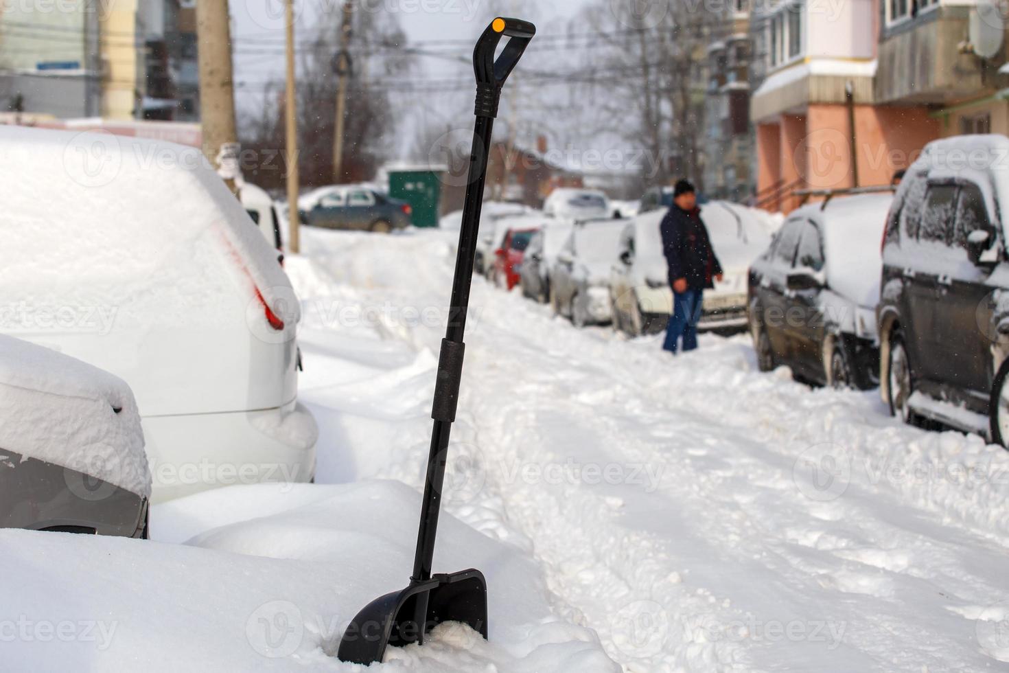 big black plastic snow shovel near snow-covered cars at sunny winter morning photo