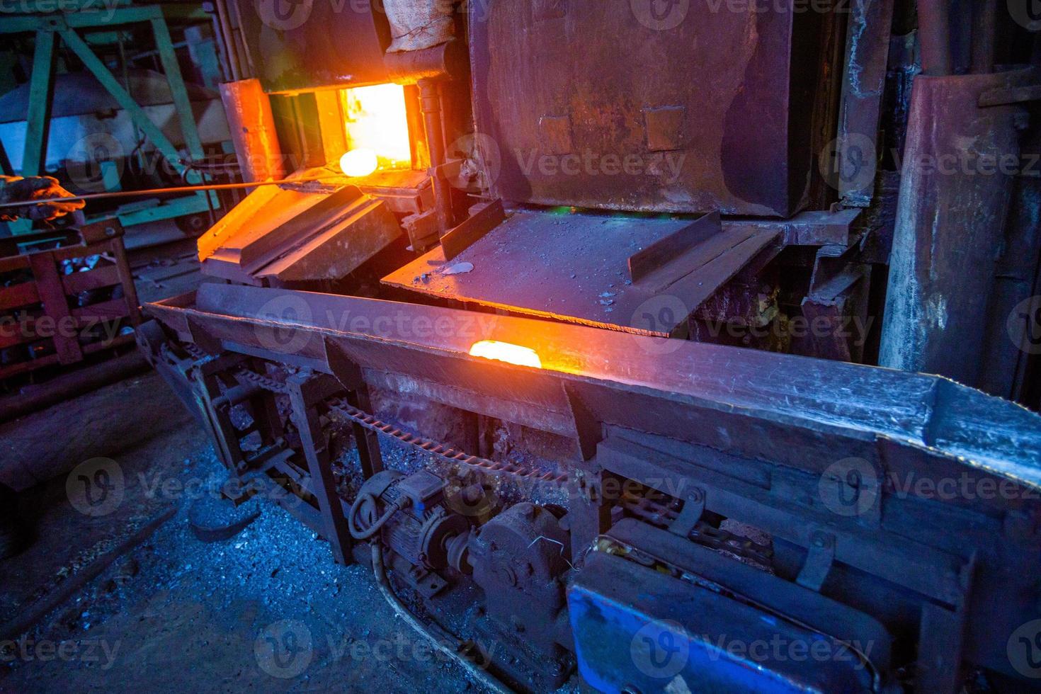 A process of moving luminous hot steel workpiece from furnace to hammer with chain conveyor. photo