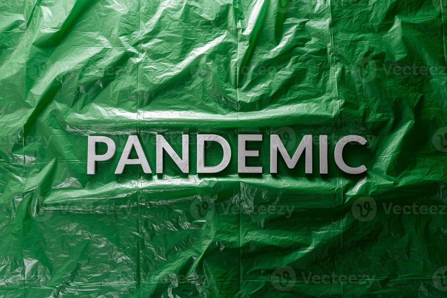 the word pandemic laid with silver letters on green crumpled plastic film background in flat lay composition at center photo