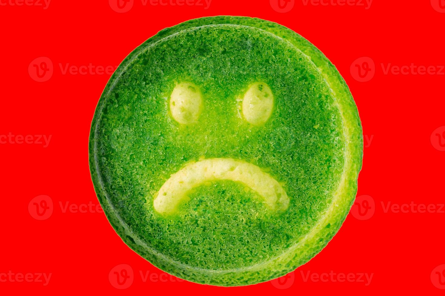 unhappy green face biscuit cookie isolated on red background in flat lay perspective photo