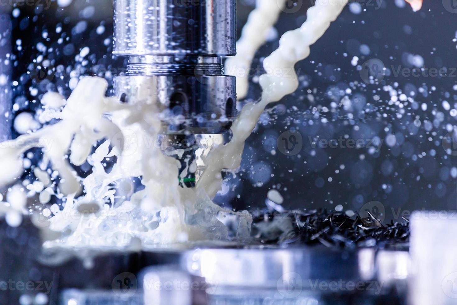 Close-up view of vertical cnc steel milling process with external water coolant streams, splashes and a lot of metal chips, high contrast photo