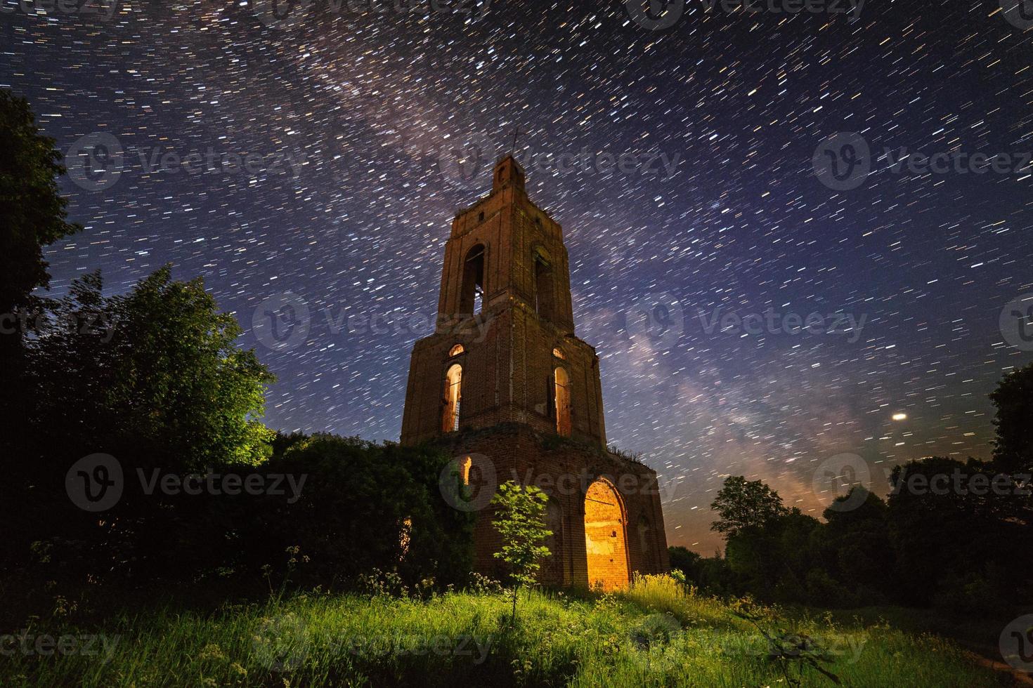 night bell tower ruin in forest at starry night with internal light photo