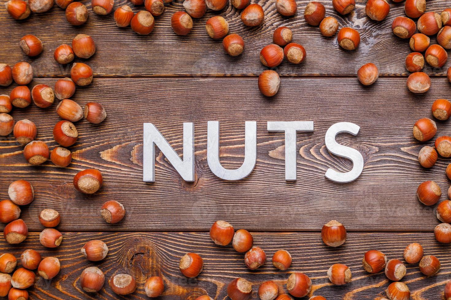 the word nuts laid with silver letters on wooden board background surrounded with scattered hazelnuts photo