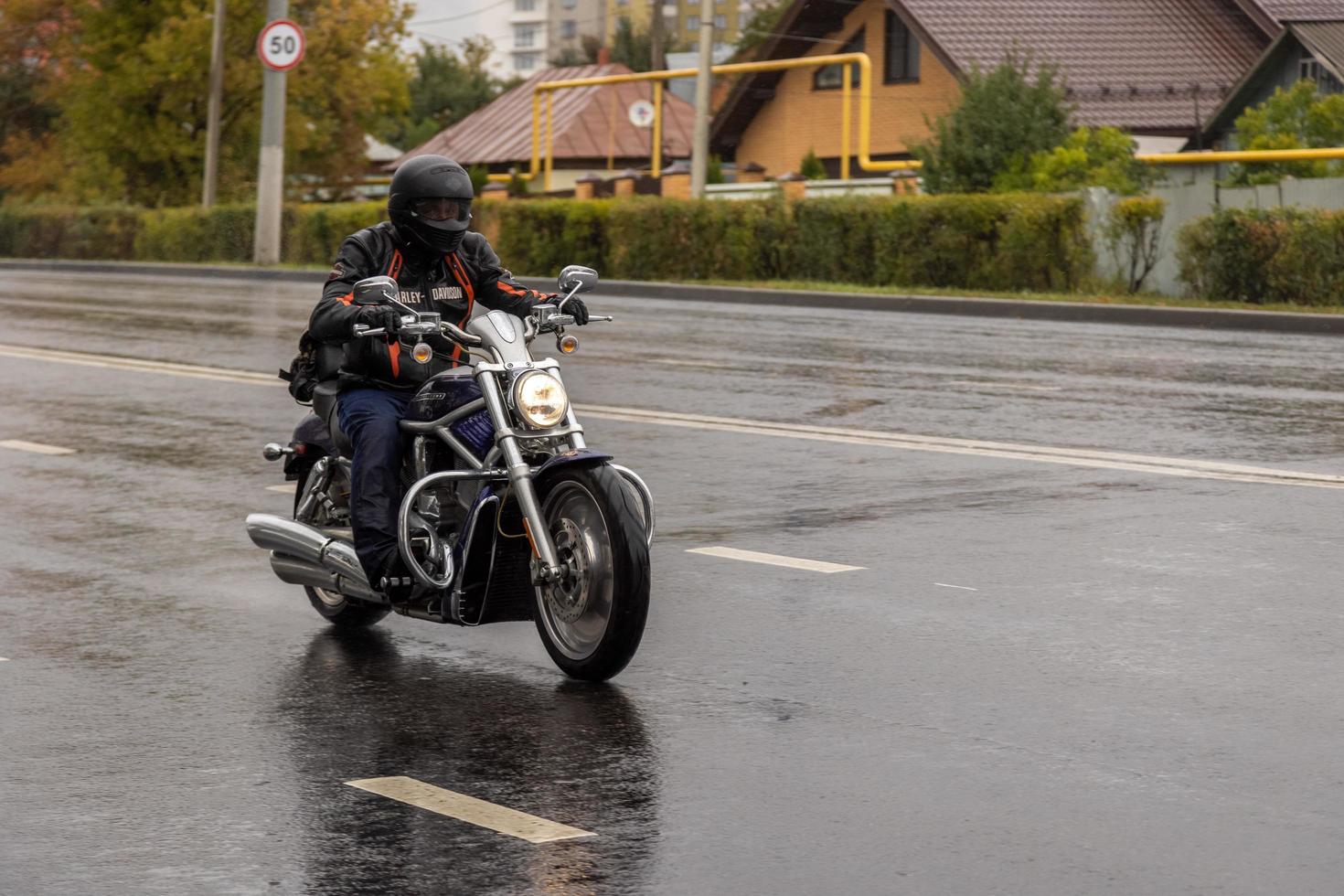 hombre en bicicleta chopper negra moviéndose en el camino húmedo del suburbio de otoño foto