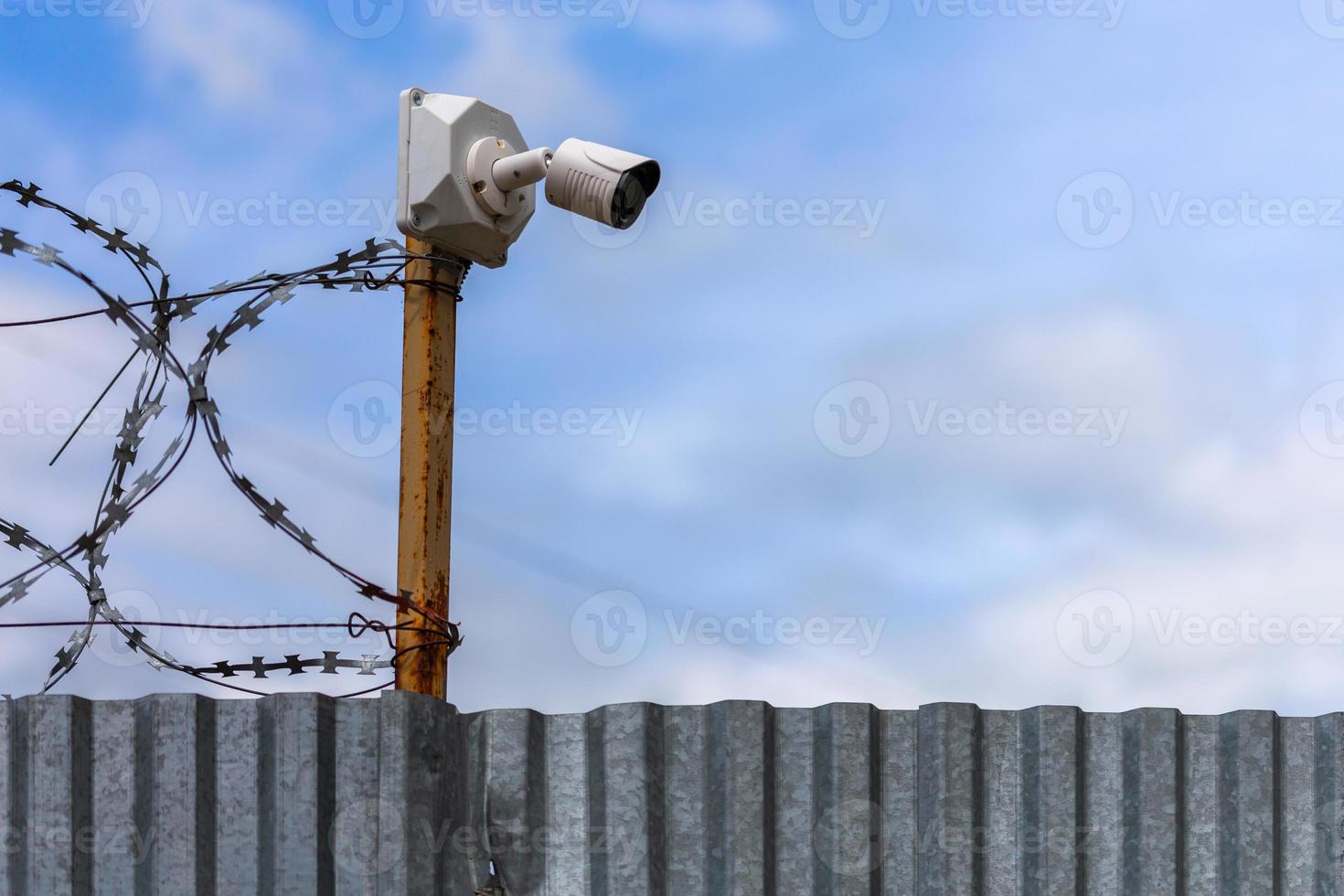 Profiled sheet fence with cheap surveillance camera and barbwire with selective focus. photo