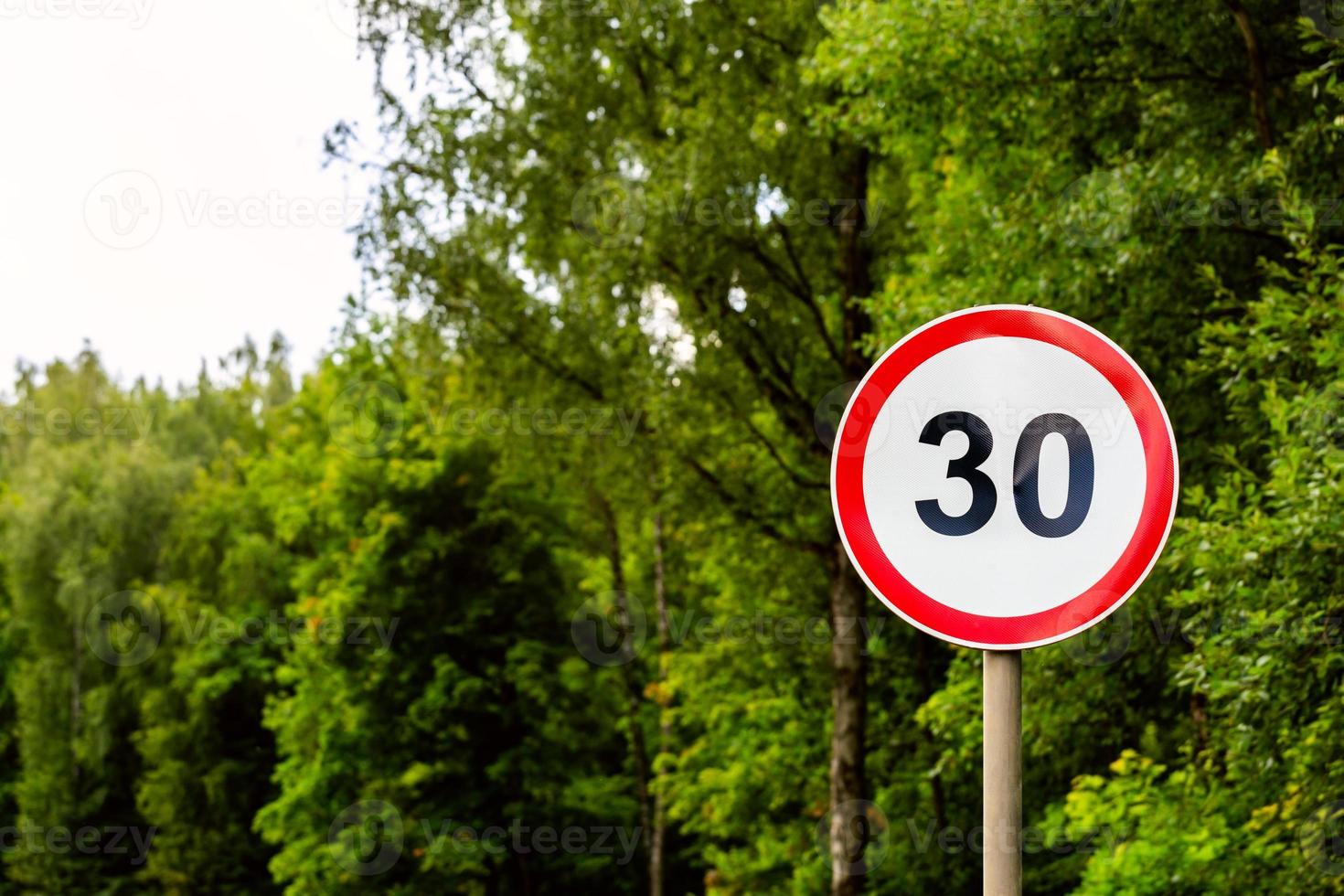 Road sign speed limit 30 kilometers per hour on green forest background with selective focus photo