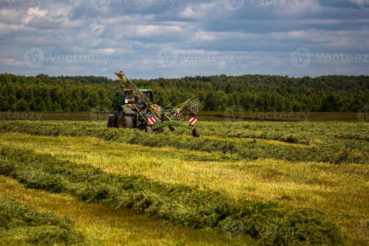 green haymaking tractor on summer field before storm - telephoto shot photo