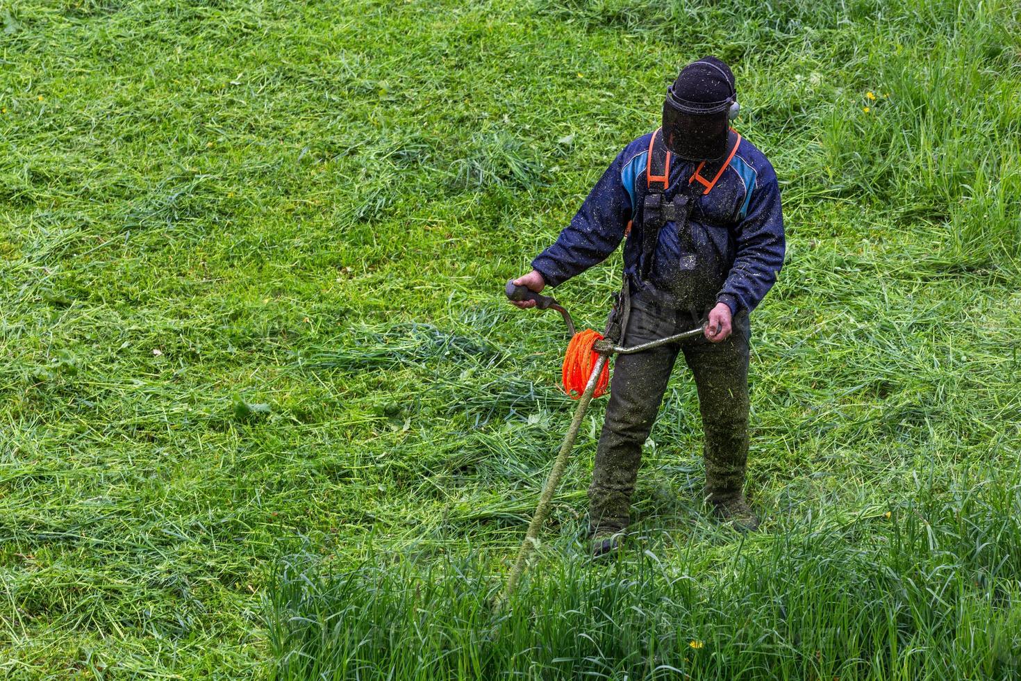 lawnmower man with string trimmer and face mask trimmong grass - close-up photo