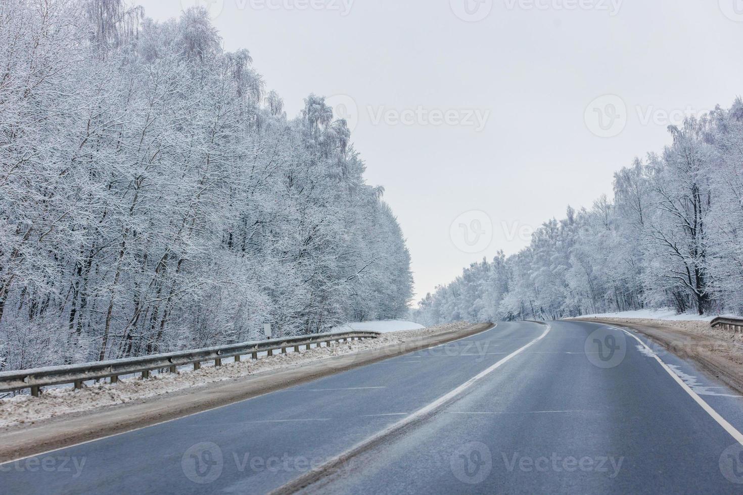 winter road among frosted forest at daylight with no cars on it photo