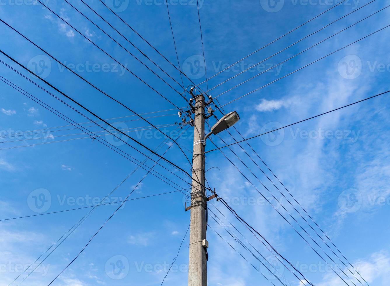 poste de luz de hormigón con muchos cables conectados radialmente en el cielo azul con nubes de plumas en el fondo, composición centrada. foto