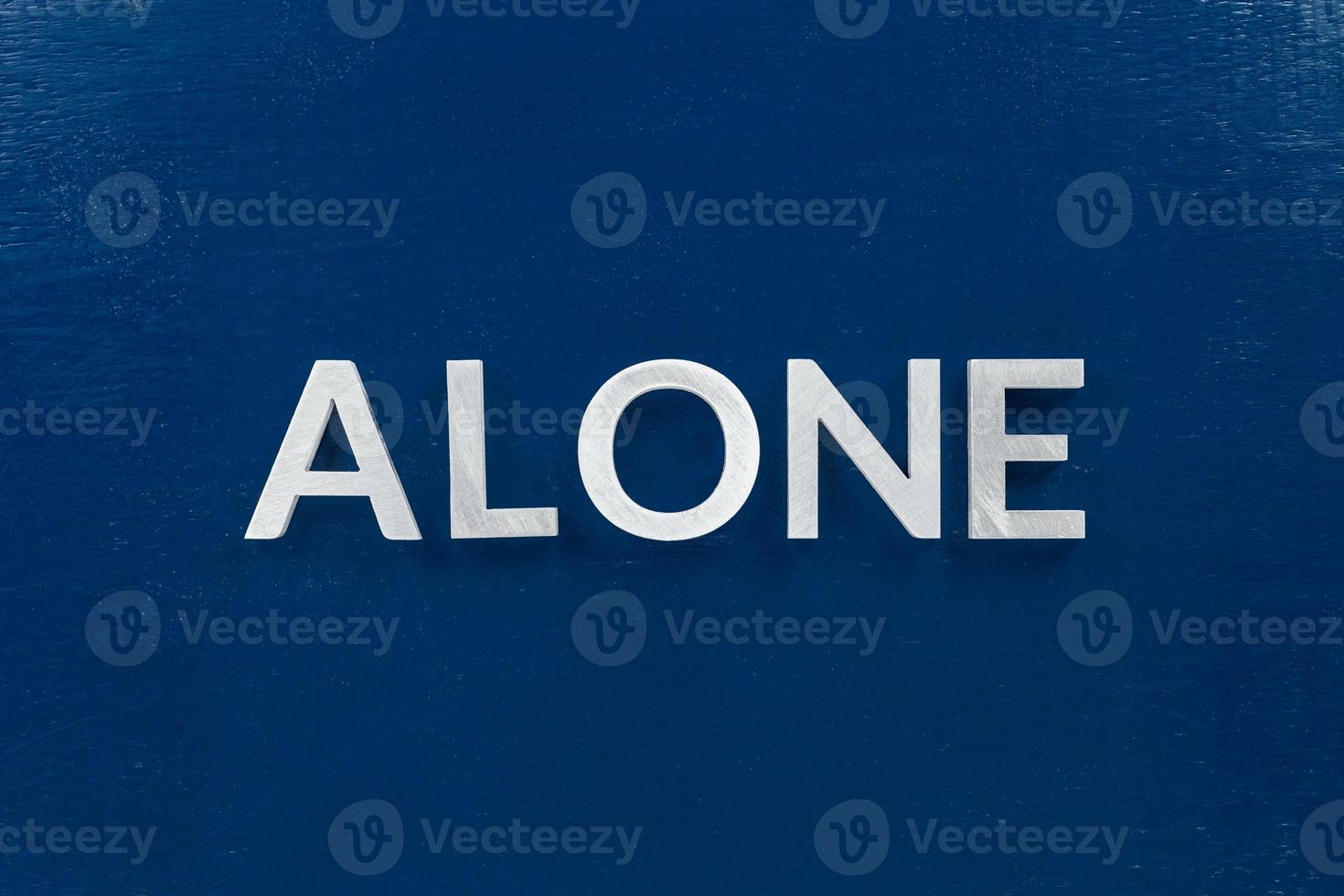 The word alone laid with silver metal letters in center of painted classic blue flat board. View in flat lay perspective. photo