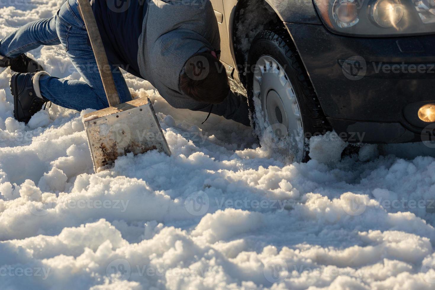 man working at car stuck in snow on knee with shovel at daylight offroad photo