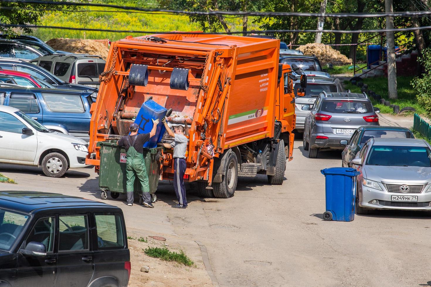 tula, rusia 27 de julio de 2019 dos trabajadores cargando basura en un camión de basura en el estacionamiento foto