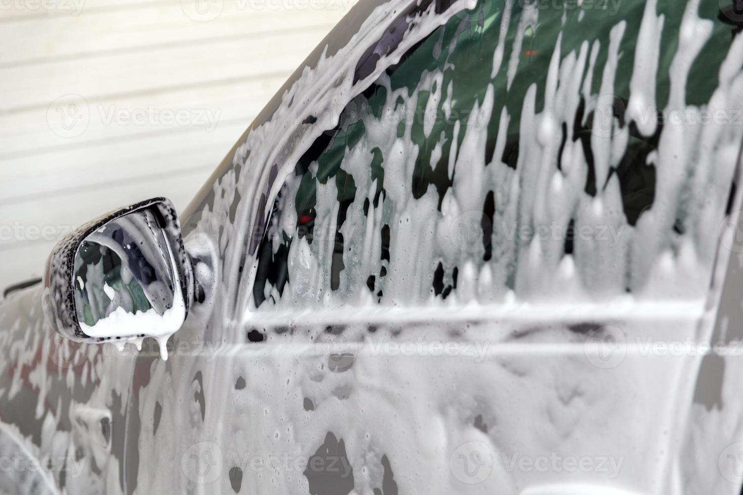 vista de cerca de la ventana del automóvil con una capa de espuma de jabón durante el lavado de automóviles. foto