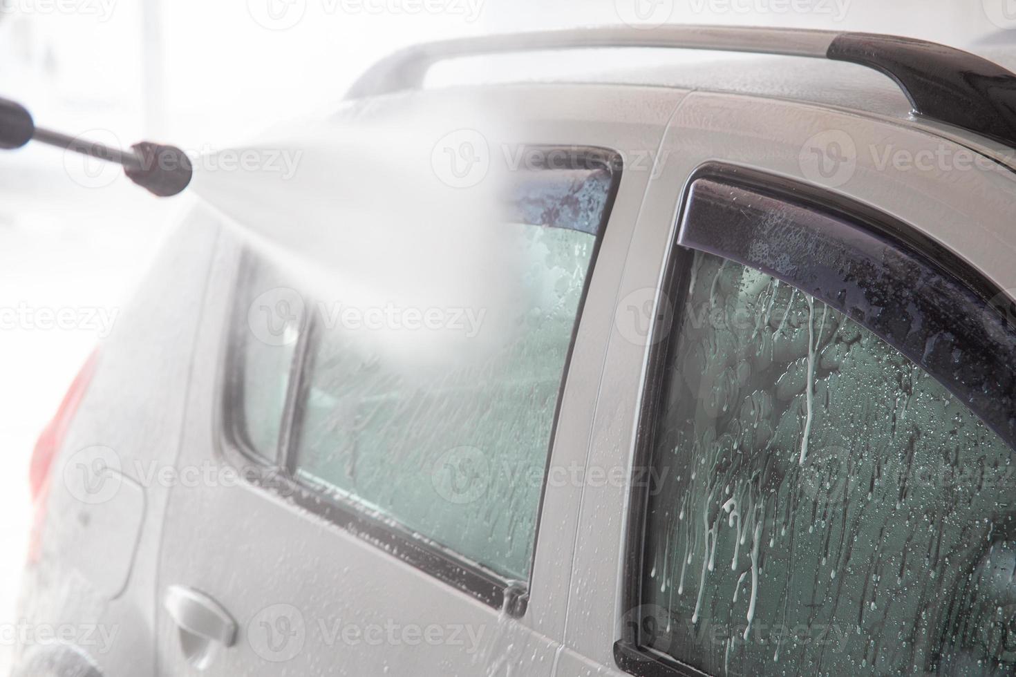 un proceso de enjuague de espuma de jabón en la ventana plateada del automóvil con corriente de agua presurizada en la estación de lavado de automóviles interior de autoservicio foto