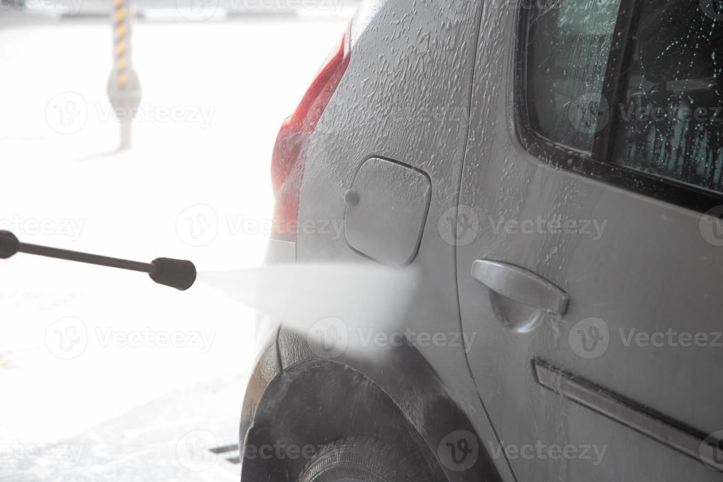 un proceso de enjuague con espuma de jabón en un automóvil plateado con un chorro de agua a presión en una estación de lavado de autos interior de autoservicio foto