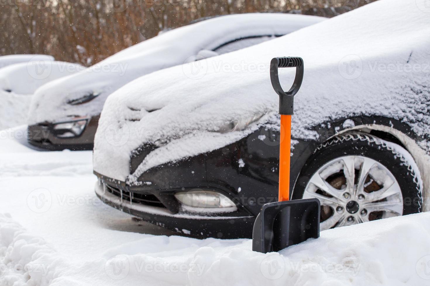 plastic snow shovel in front of snow-covered car at sunny winter morning photo