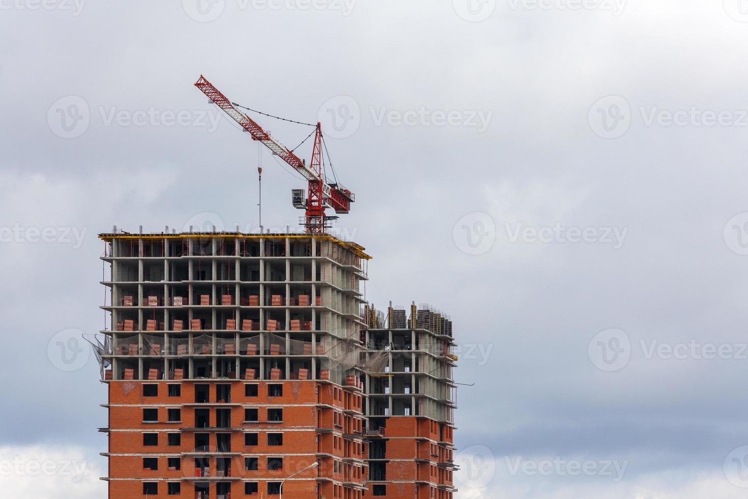 building process of large residential apartment building with crane on cloudy sky background photo