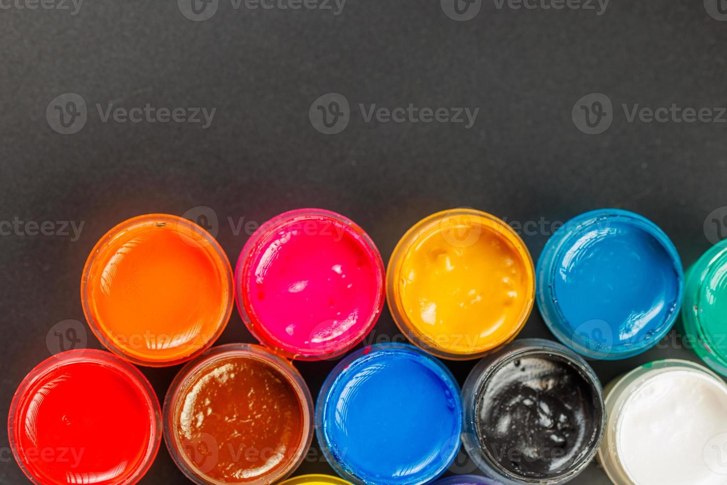 close-up background of opened small gouache paint jars on black surface photo