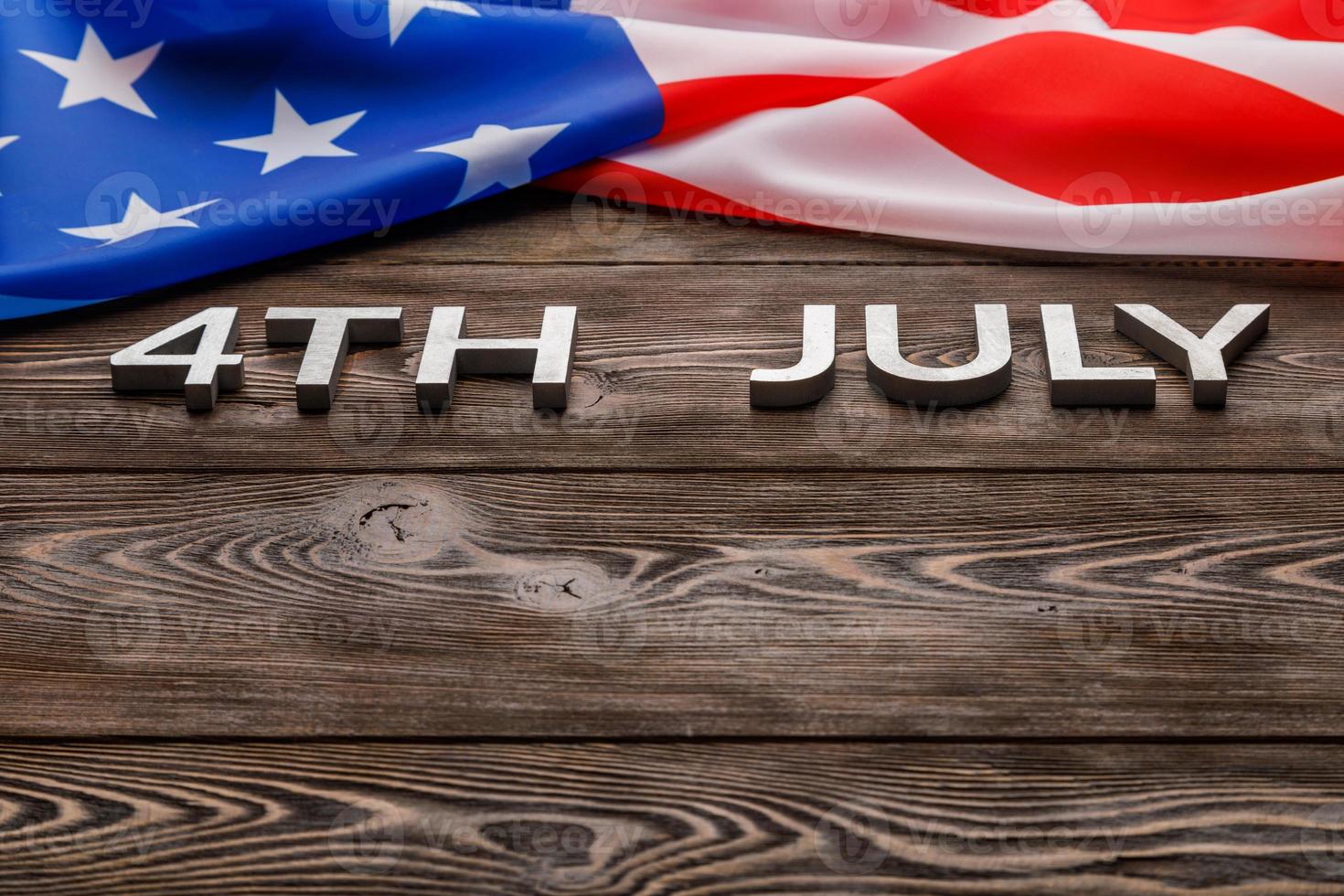 words 4th july and crumpled usa flag on flat textured wooden surface background photo