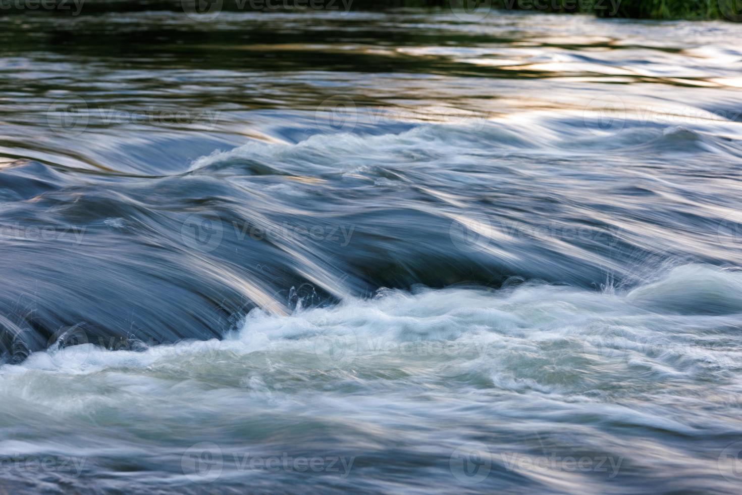 agua que fluye de un río de verano con una pequeña cascada rápida a la luz del atardecer foto