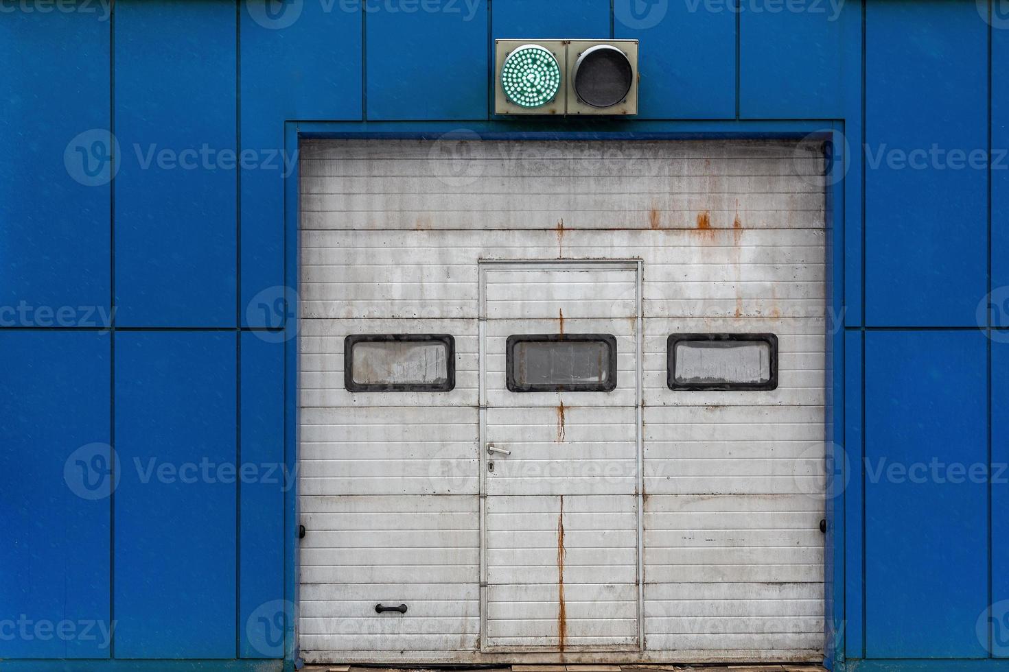 a white automatic upward sliding gate on blue garage with green lit traffic light photo